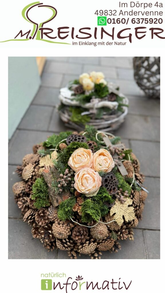 Ein dekorativer Kranz aus Kiefernnadeln, Zapfen, Trockenblumen und grünem Moos, mit zarten rosafarbenen Rosen in der Mitte, auf einem gepflasterten Boden. Im Hintergrund ist ein weiterer Kranz zu sehen, der auch natürliche Elemente enthält.