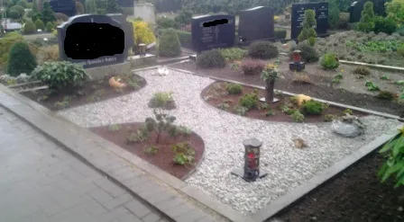 Trauerstätte mit Steinen, Pflanzen und Grabsteinen, umgeben von gepflegtem Grün und dekorativen Lichtern.